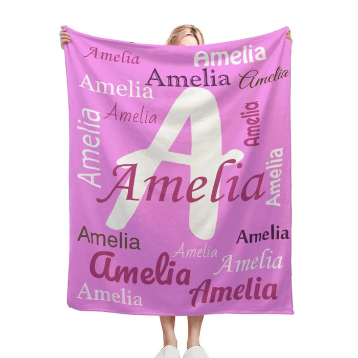 Square pink throw blanket with white letter A and repeated Amelia name