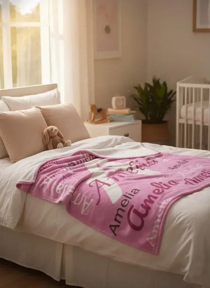 Pink fleece throw blanket with Amelia name pattern on a bed