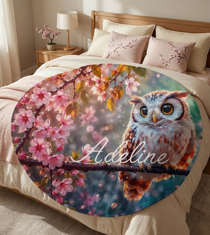 Round owl throw blanket spread on a bed with owl and pink cherry blossom print
