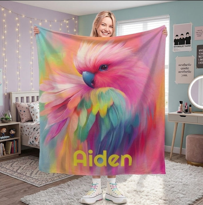 Personalized rainbow parrot name blanket held up with 'Aiden' in yellow.