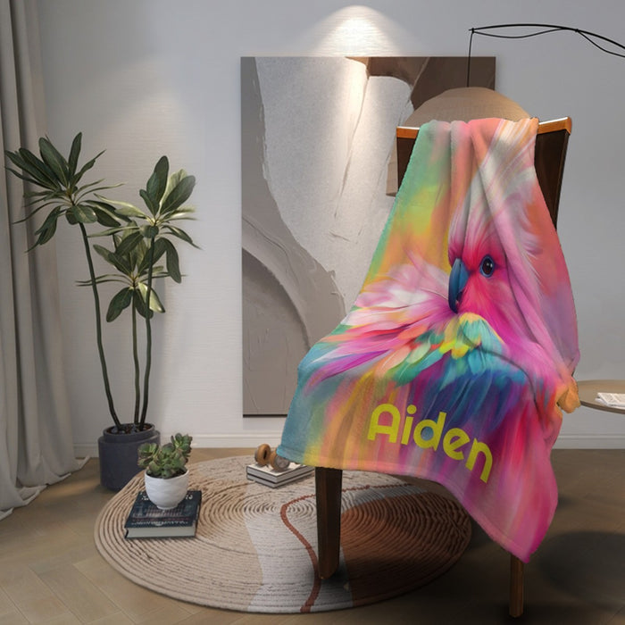 Rainbow parrot blanket hanging on chair, 'Aiden' text over colorful feather artwork.