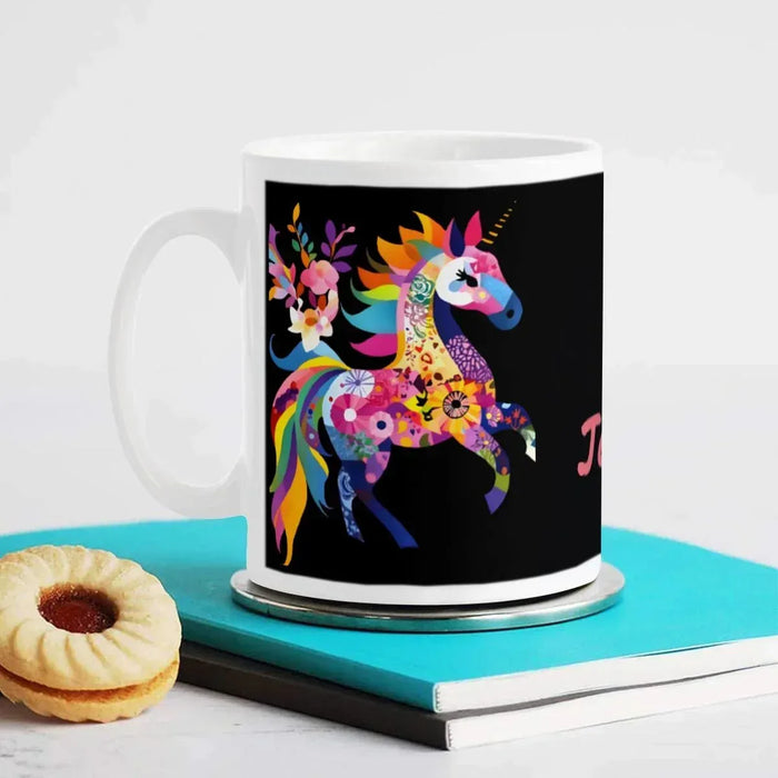 Black ceramic mug with rainbow unicorn illustration; white rim, on teal tray