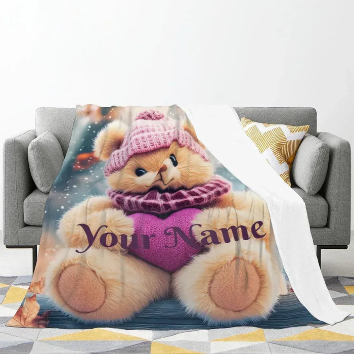 Personalized teddy bear plush blanket spread over a couch, “Your Name” printed.