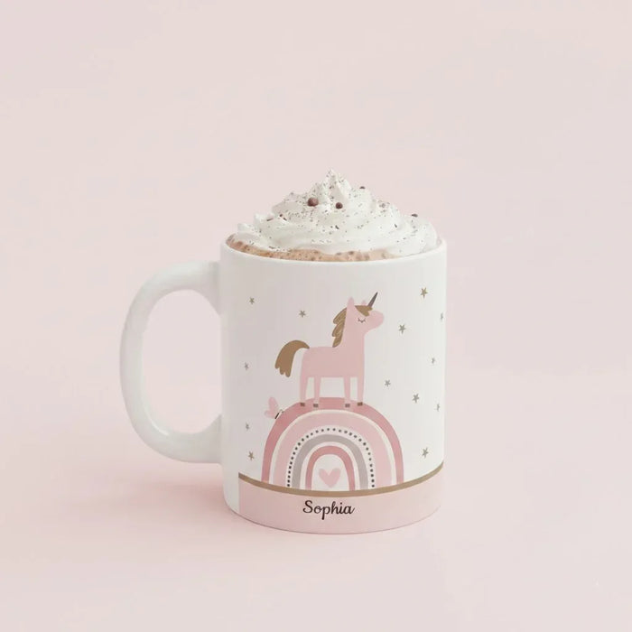 White ceramic mug with unicorn and pink rainbow design, topped with whipped cream