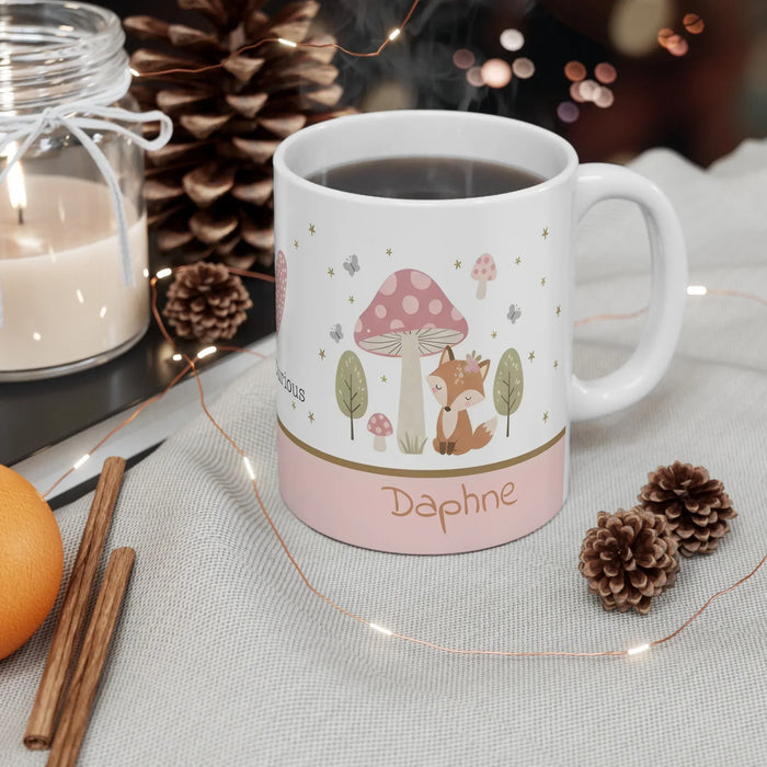 White ceramic mug with fox-and-mushroom illustration and 'Daphne' name, hot drink inside