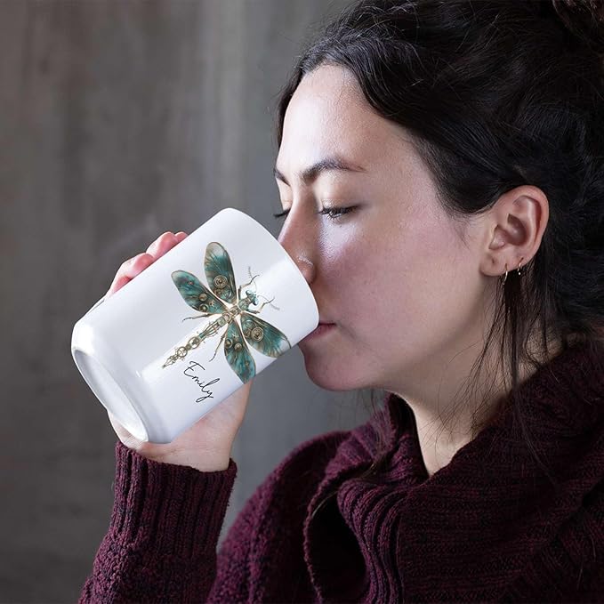 White ceramic mug with teal steampunk dragonfly and name Emily, held near lips