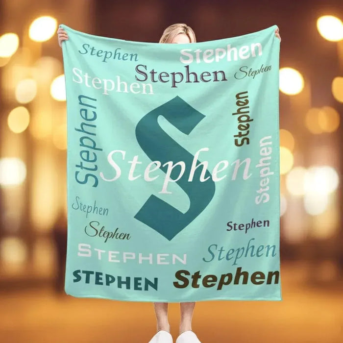 Mint green personalized blanket with repeating navy “Stephen” lettering pattern.