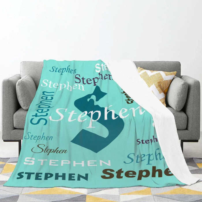 Mint green personalized blanket draped over a couch with navy “Stephen” name print.