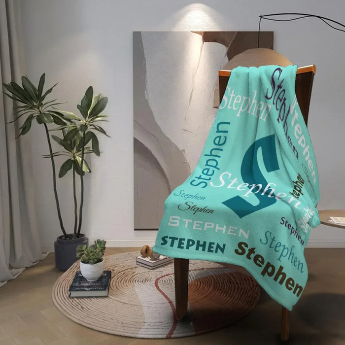 Mint green personalized blanket draped over a chair with navy “Stephen” lettering.