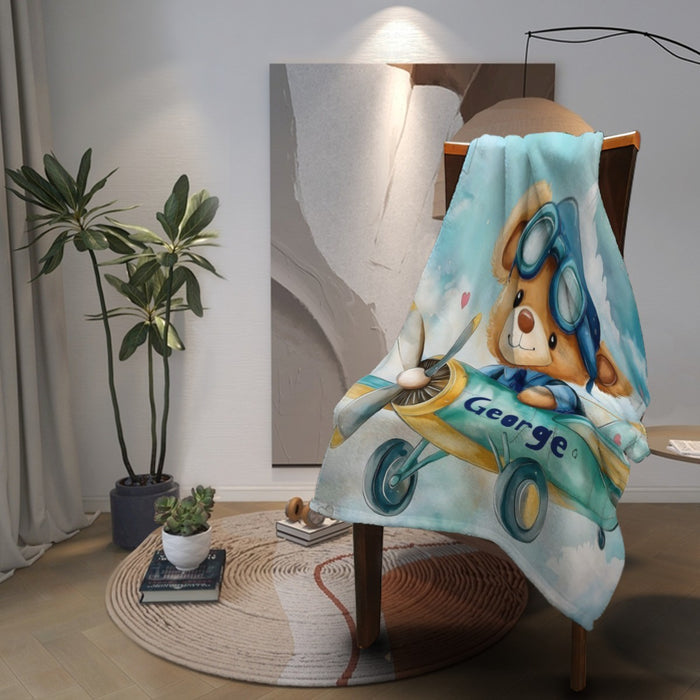 Draped pilot teddy bear blanket showing blue goggles, airplane wings, and George lettering