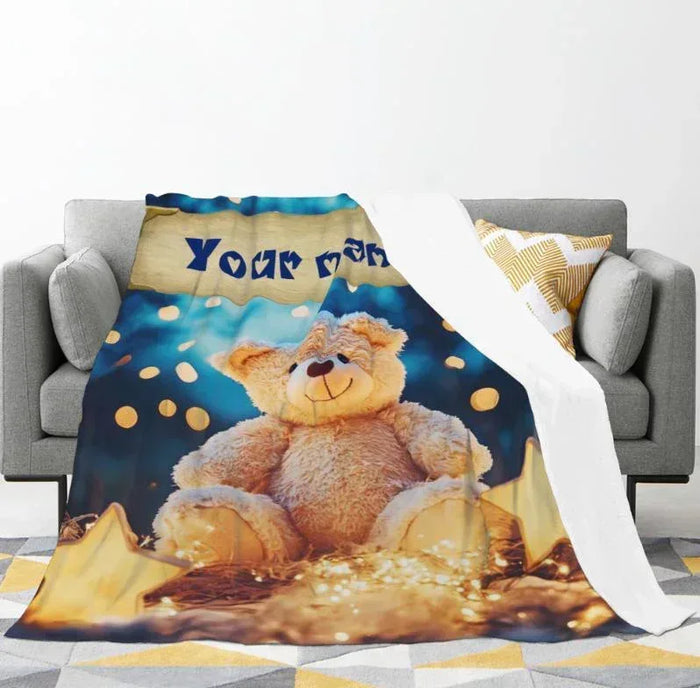 Teddy bear plush blanket draped over sofa, blue star print with teddy and name band