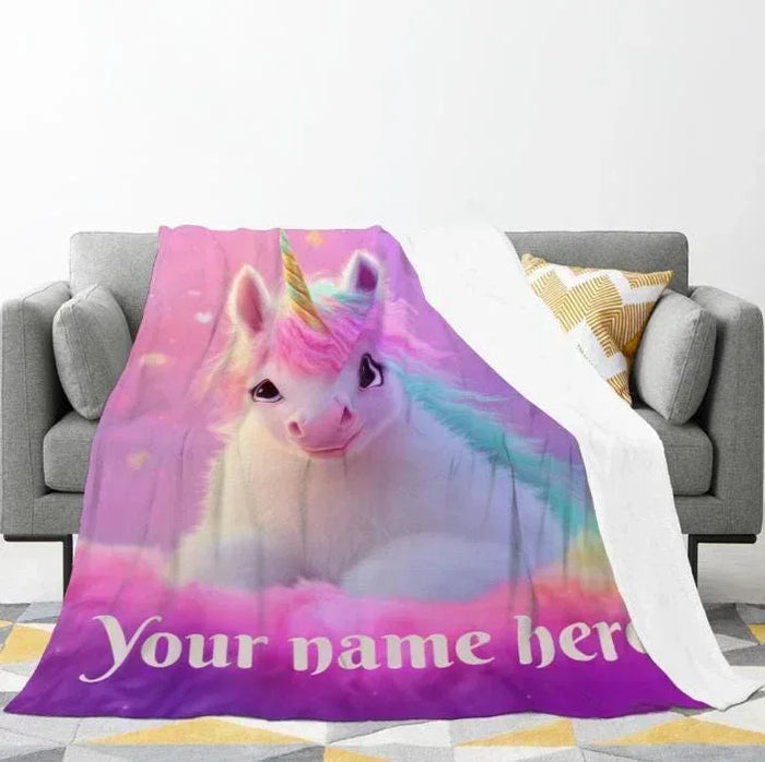 Unicorn fleece throw blanket on sofa, rainbow mane and white unicorn face with name text.
