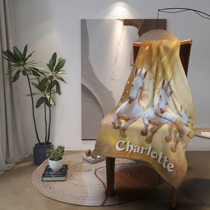 Personalized unicorn name blanket with three white horses and “Charlotte” over chair