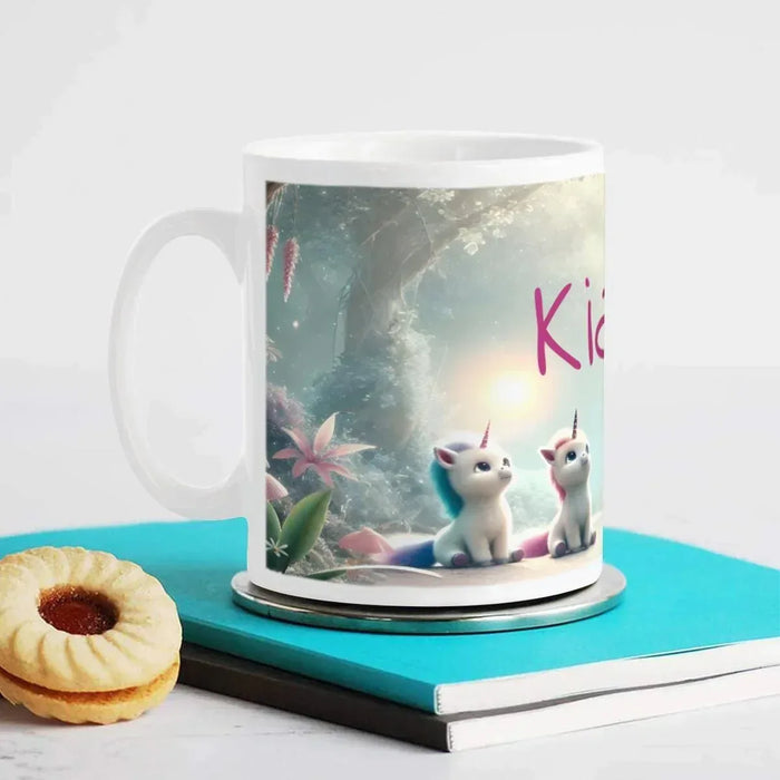White mug with handle on a book; unicorn kittens in a forest scene and partial Kiara text