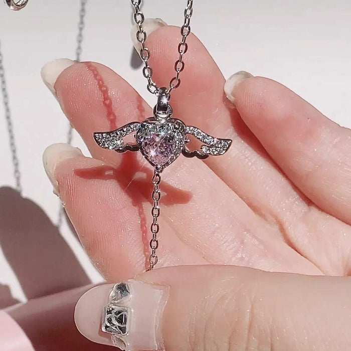 Silver-tone angel wings heart pendant necklace with pink crystal heart shown in palm