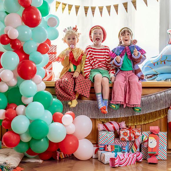 Balloon cluster with pink, green, and red balloons and gift boxes with seated children