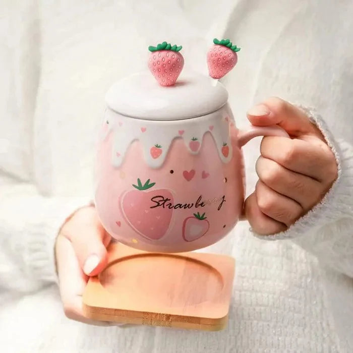 Pink ceramic lidded mug with strawberry topper held in hand; strawberry heart pattern