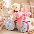 Pink tricycle diaper cake gift basket with plush bear and blue diaper wheels, ribbons