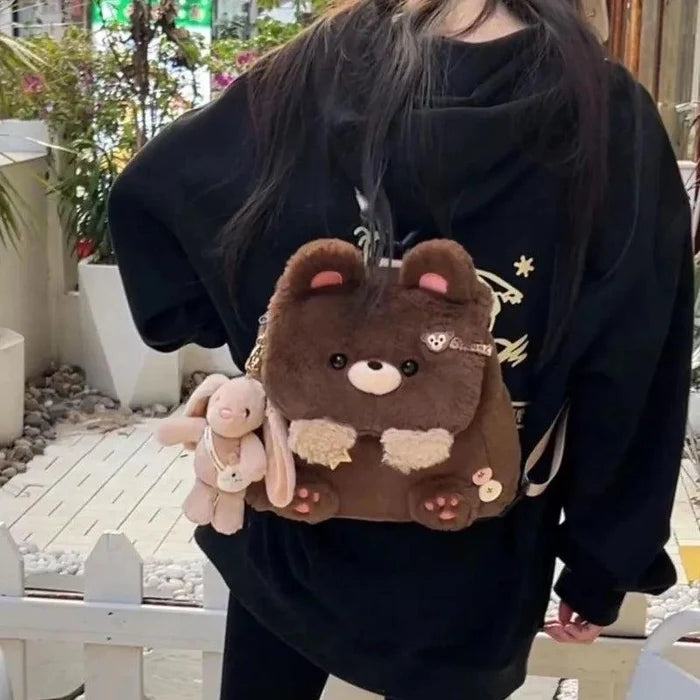 Plush teddy bear bag in brown held by person, bunny charm on side