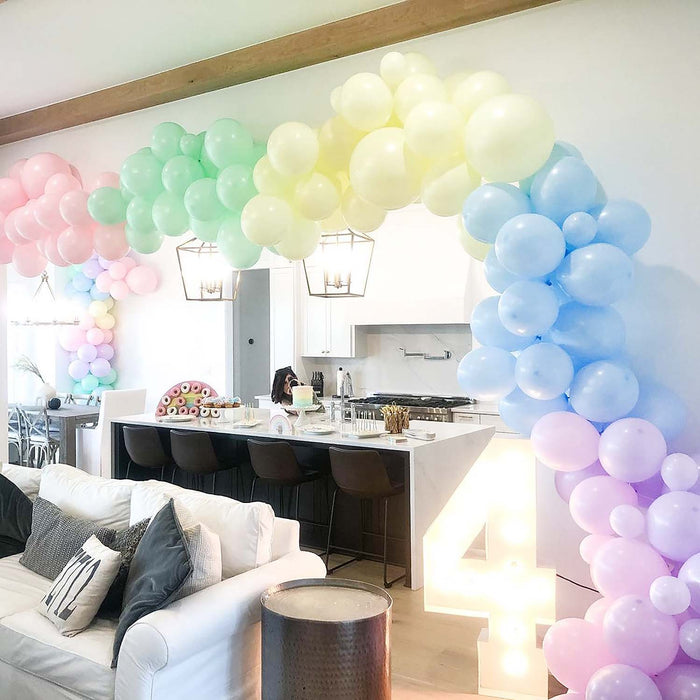Pastel balloon clusters in blue, lilac, green, pink, and yellow around a party table