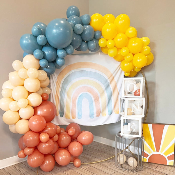 Balloon arch with slate blue, yellow, cream, and terracotta balloons