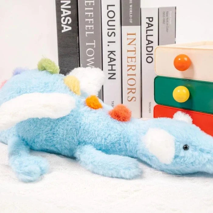 Light blue plush dragon lying on white with multicolor belly spots and black eyes