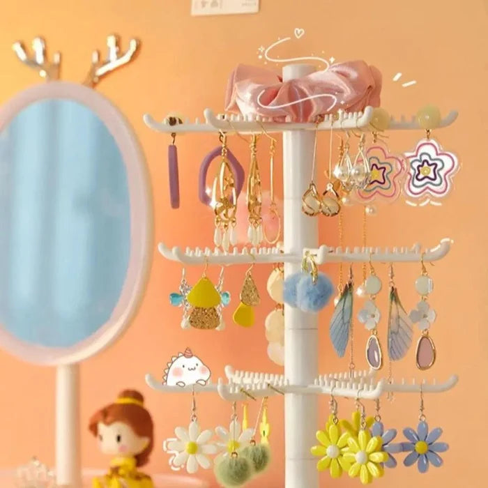 White rotating earring stand with hoop and dangling earrings hanging from hook tiers