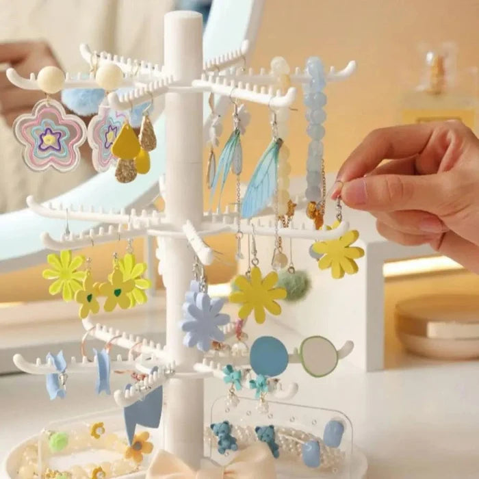 White multi-tier earring stand with flower and dangling earrings, hand reaching