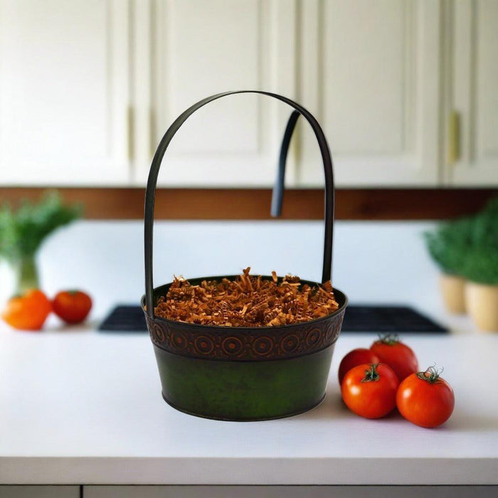 Green gift basket with black handle, filled with brown shredded filler on a countertop