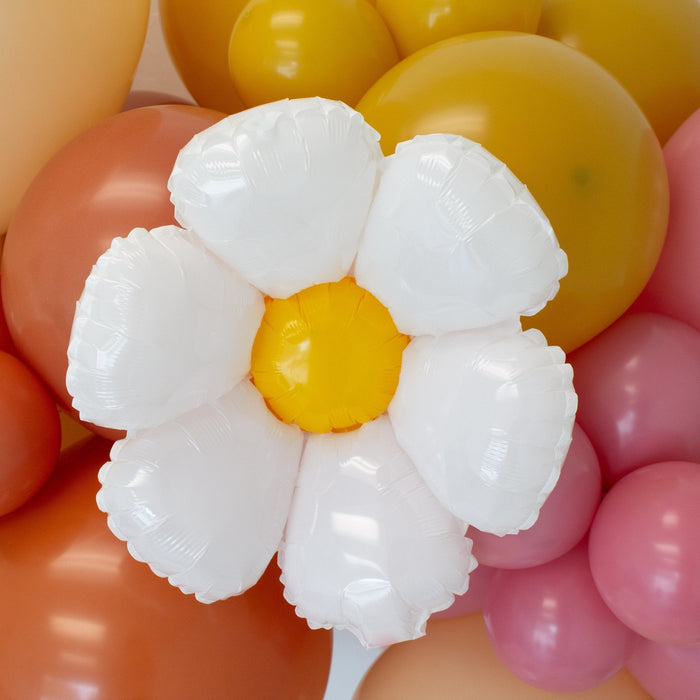 White daisy foil balloon with yellow center nestled among yellow, pink, and orange balloons
