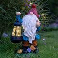 Outdoor gnome garden statue, red hat and white beard, blue coat, holding glowing solar lantern