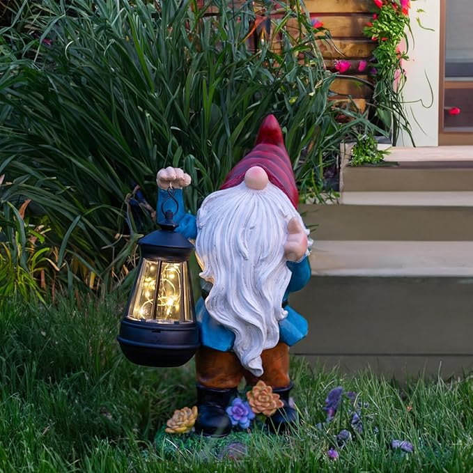 Garden gnome statue with red pointed hat, white beard, blue coat, holding solar lantern by plants