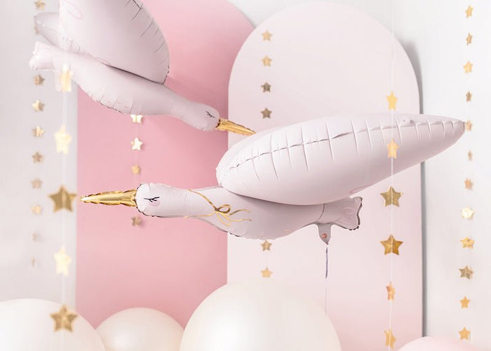 Stork balloon close-up in pale pink and white with gold beak, hanging with small stars.