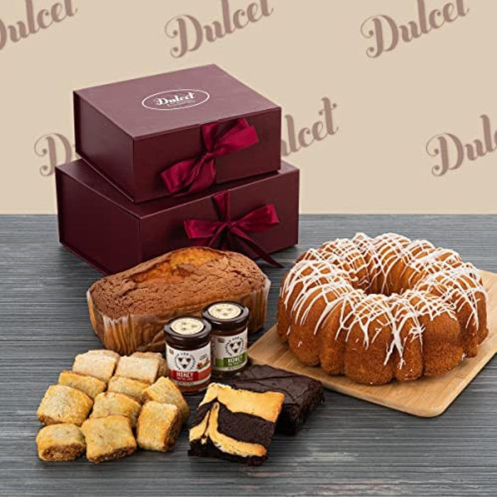 Two-tier gourmet gift box with dark maroon lids and satin bow, open with assorted pastries