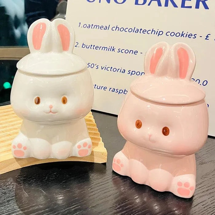 Pair of ceramic bunny-lid mugs, one white and one pink, with ear and paw details