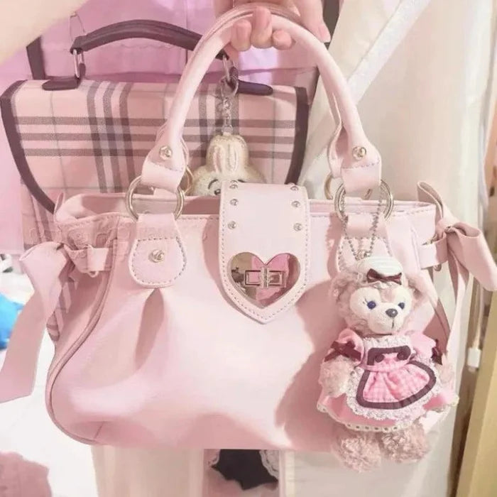 Pink heart-lock handbag with top handles, studded front crest, ribbon ties, teddy charm