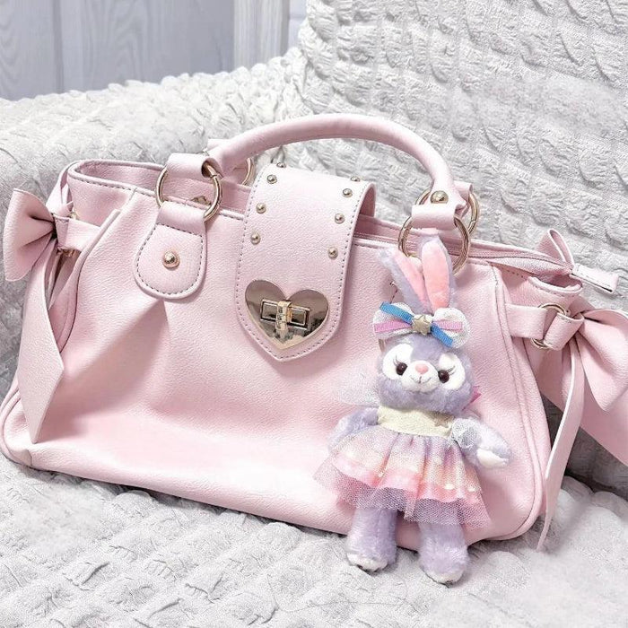 Pink heart-lock handbag with bow ties, studded panel, and bunny plush keychain charm