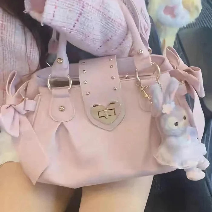 Pink heart-lock handbag close-up with heart crest, gold studs, and ribbon-trim side details