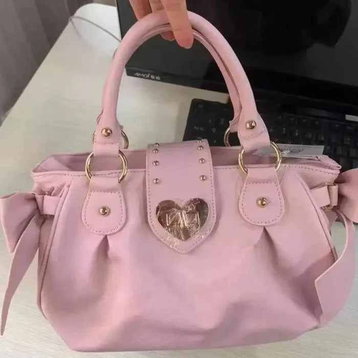 Pink heart-lock handbag with gold heart crest, studded front panel, and ribbon bow ties