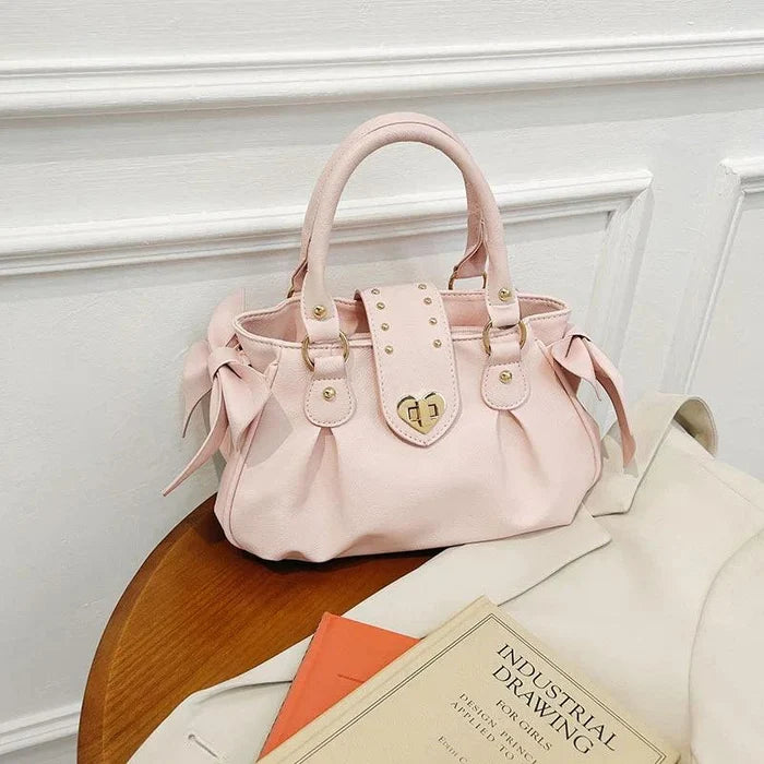 Pink heart-lock handbag with twin handles, ribbon ties, and studded front emblem