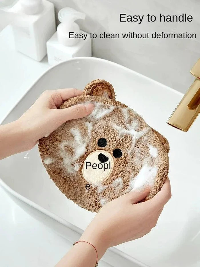 Brown teddy bear hand towel with bear face and plush texture, used on a sink