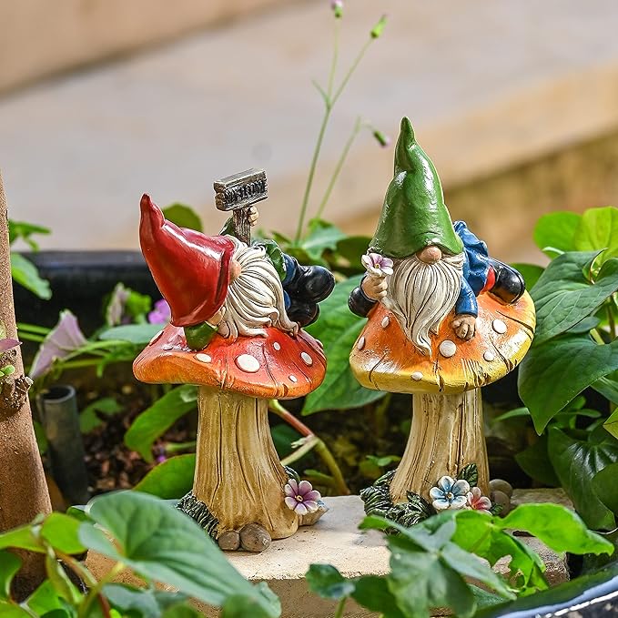 Resin garden gnome statues set of 2 standing among green plants, red and green hats