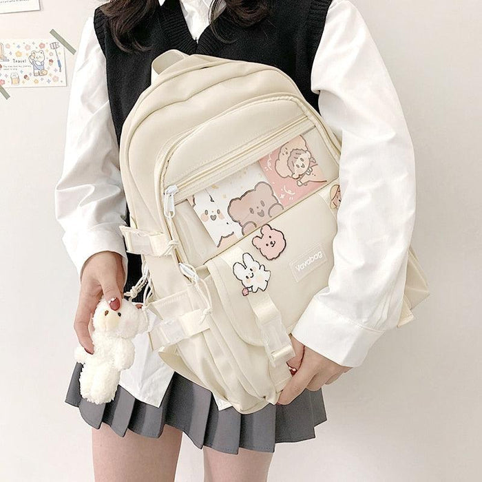Beige mini backpack with front zip pocket, cartoon patch, and dangling plush keychain