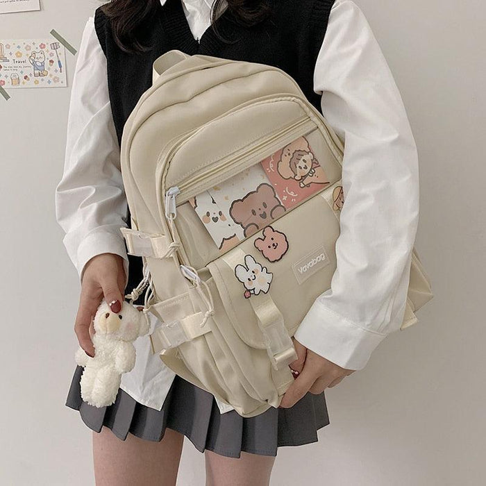 Cream mini backpack with front zip pocket, cartoon graphic panel, and front buckle straps