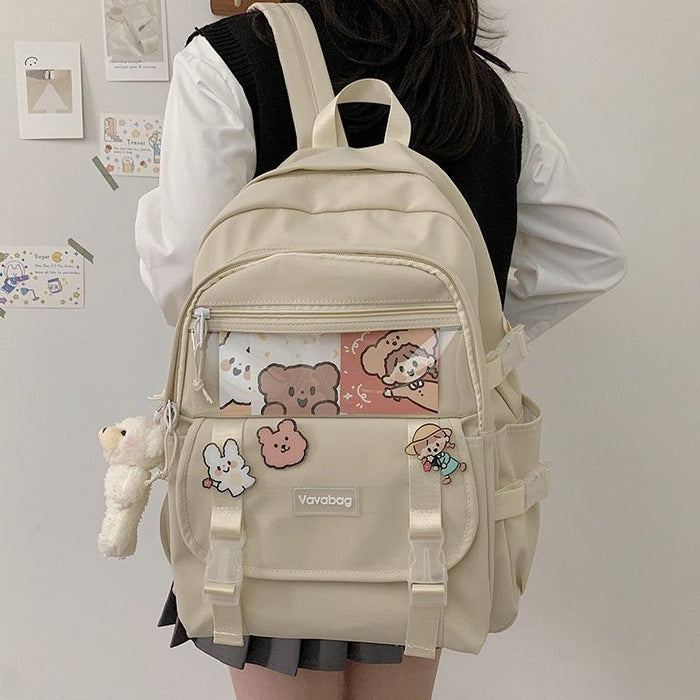 Beige mini backpack with front zip pocket, cartoon patch, and white plush hanging charm