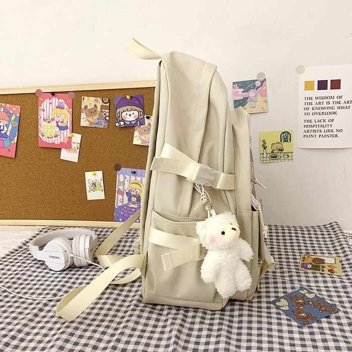 Cream mini backpack standing upright with adjustable straps and hanging plush keychain