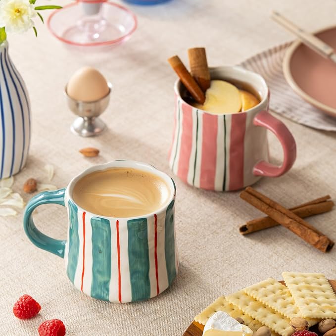 Striped ceramic coffee mugs, teal and pink with red and white vertical stripes, on table