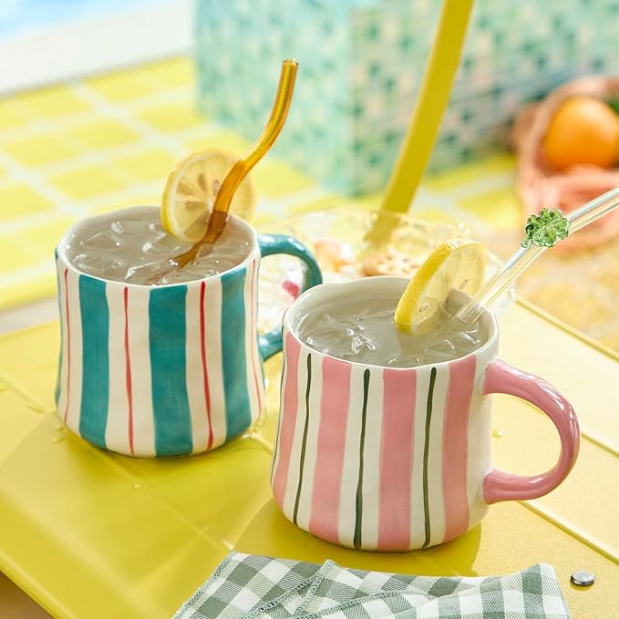 Two ceramic coffee mugs with teal and pink vertical stripes, lemon drinks with straws