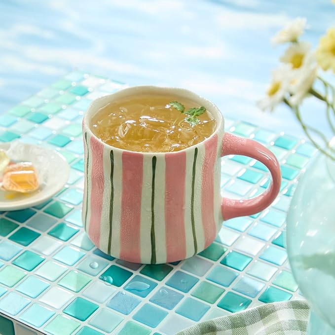 Ceramic coffee mug with vertical pink, white, and green stripes, filled with tea
