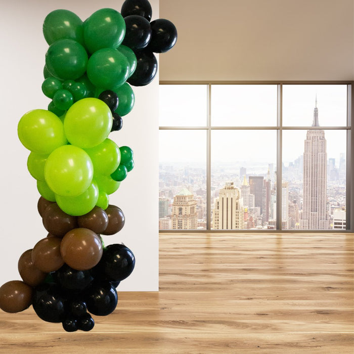 Tall balloon garland column with green, lime, brown, and black balloons near window